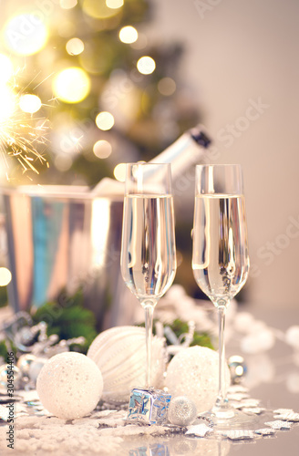 Christmas and New Year celebration with champagne. Holiday dinner table setting with Christmas tree decoration, two flutes of sparkling wine on served table, holiday Xmas dinner. Champagne