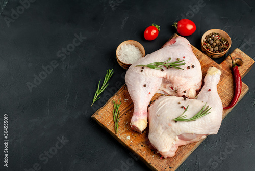 Raw chicken legs with spices and herbs, ready for cooking on a stone background, with copy space for your text.