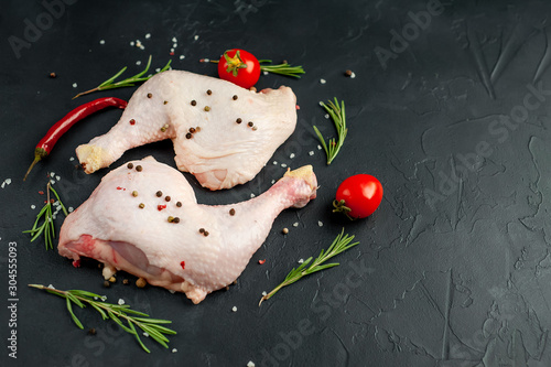 Raw chicken legs with spices and herbs, ready for cooking on a stone background, with copy space for your text.