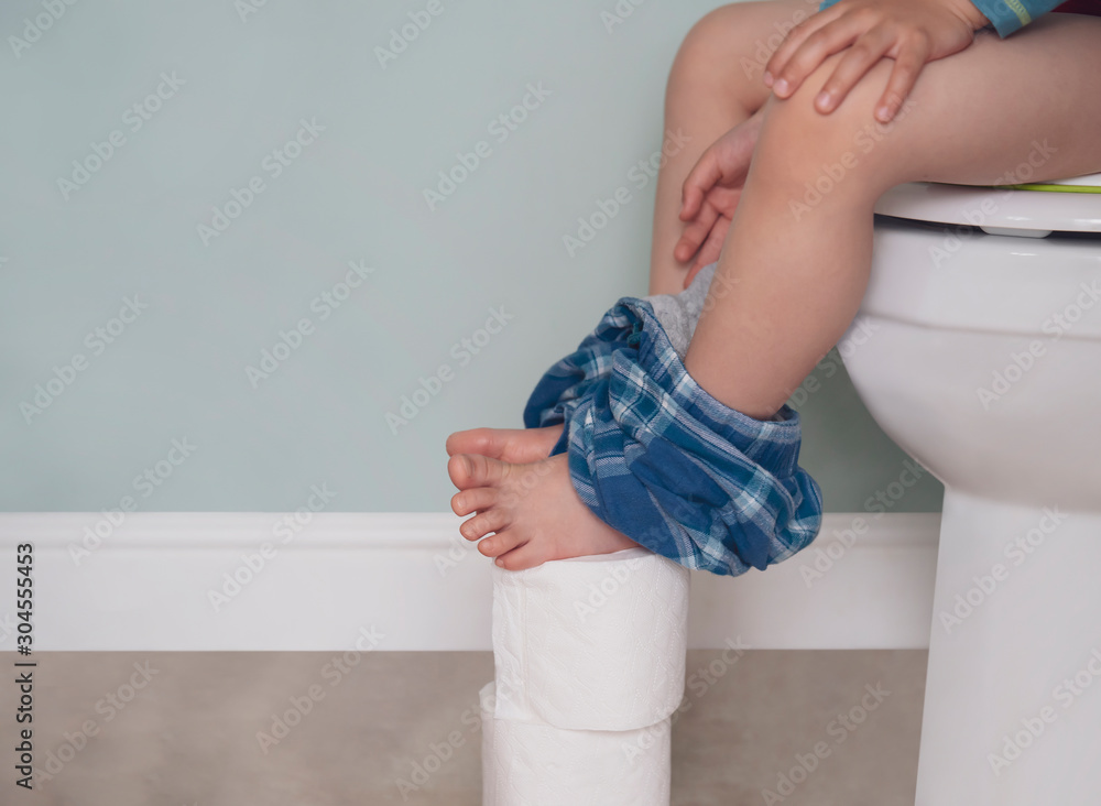 Preschool kid sitting on toilet putting his feet on toilet rolls,Low