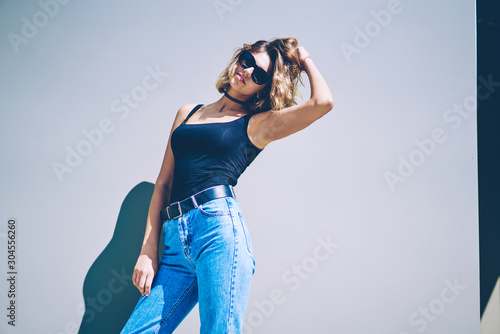 Half length portrait of attractive caucasian model posing near copy space area for advertising text, beautiful woman in trendy sunglasses looking at camera near promotional background during sunny day © BullRun