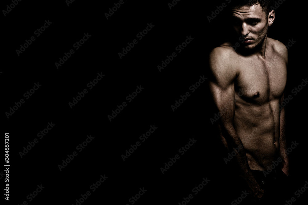 Shirtless athletic masculine man over dark black background Shirtless athletic masculine man over dark black background