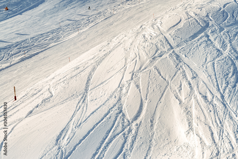 Fototapeta premium Snowy abstract off-piste skiing backround with ski and snowboard trails and tracks on new virgin powder snow. morning sunrise or evening sunset time at alpine mountain resort