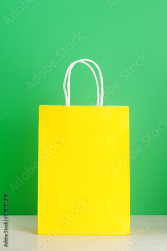 Yellow shopping or gift bag on wooden desk against green background. The concept of shopping or gifts. Layout with a copy space for your design.