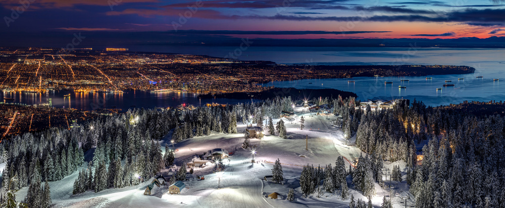 Fototapeta premium Jazda na nartach po oświetlonych stokach narciarskich Grouse Mountain z widokiem na miasto Vancouver o zmierzchu