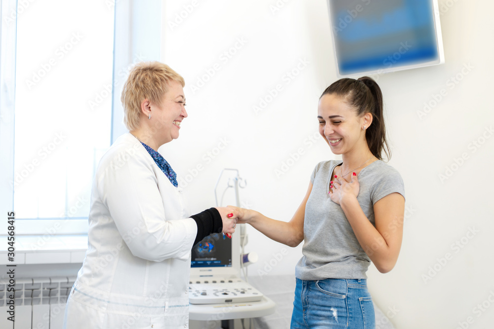 Obraz premium Happy patient shakes hands with doctor after successful ultrasound examination. In the white office of a medical clinic.