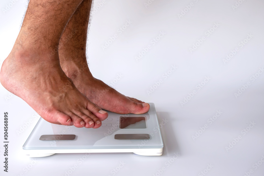 Fototapeta premium close-up of man feet on digital body fat analyzer scales on white background. fat burn and good health concept.