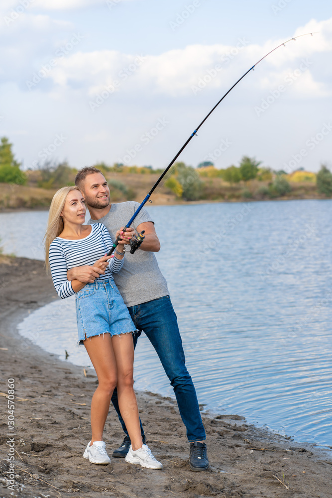 Happy young couple fishing by blue lakeside Happy young couple fishing by blue lakeside