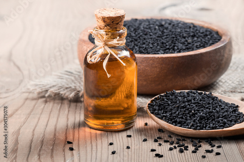 glass bottle of black cumin seeds essential oil , Nigella Sativa in spoon on wooden background. Organic herbal medicine for many diseases, texture background