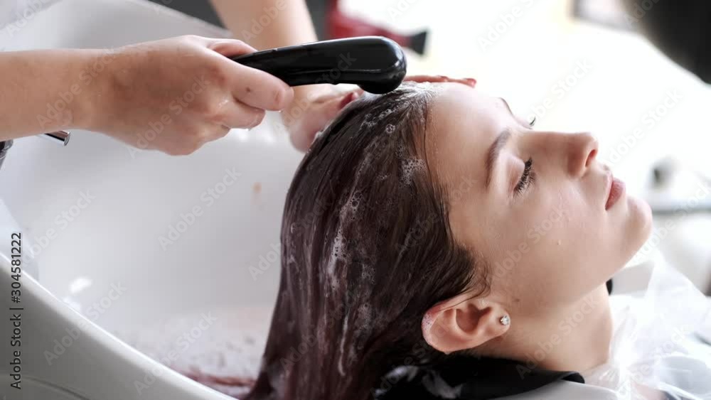 The client closes her eyes. The hairdresser washes off her head the shampoo. The sink is white. The client closes her eyes. The hairdresser washes off her head the shampoo. The sink is white.