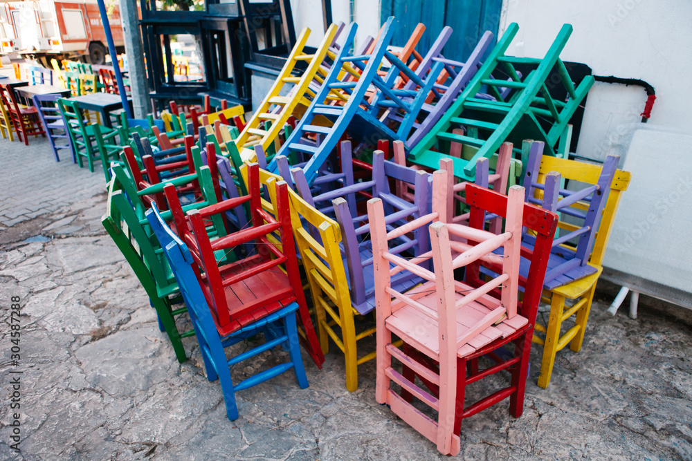 stacked colored wooden chairs. Lacquered wood chairs stacked out at a restaurant in a city street