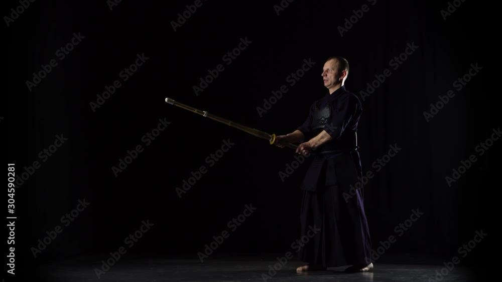 Masculine Kendo warrior practicing martial art with the bamboo bokken on black background. Masculine Kendo warrior practicing martial art with the bamboo bokken on black background.