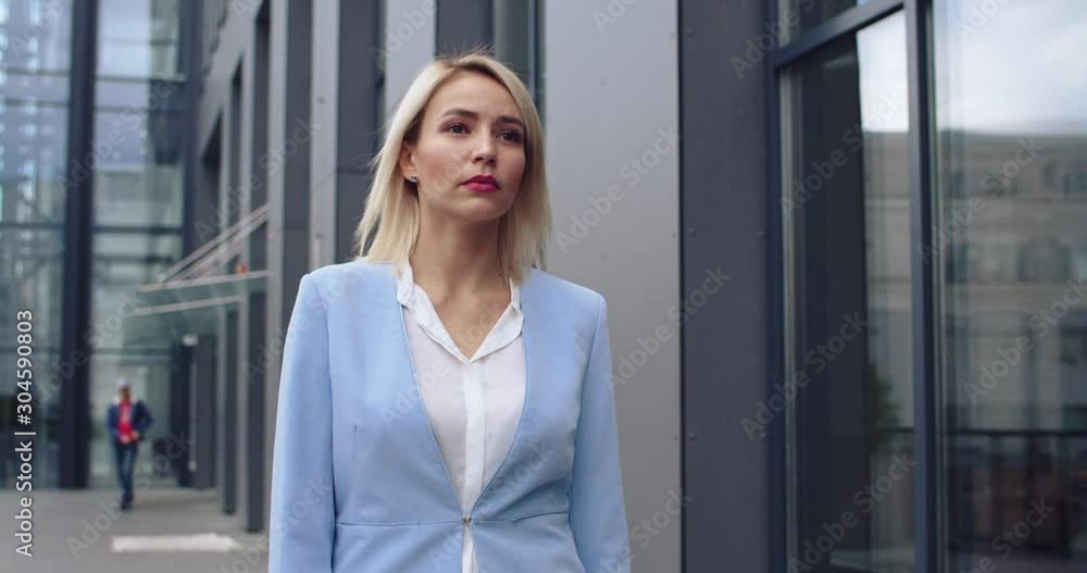 Pretty young Caucasian blonde businesswoman in stylish outfit walking outdoor while going to the office at modern building. Heading to the meeting. Pretty young Caucasian blonde businesswoman in stylish outfit walking outdoor while going to the office at modern building. Heading to the meeting.