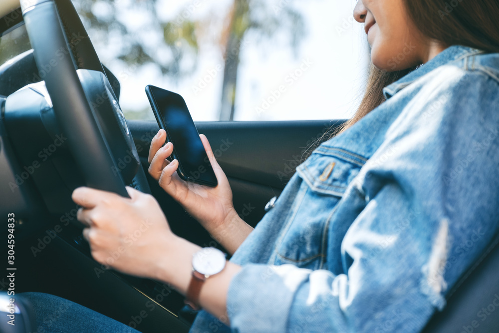 Closeup image of a woman using mobile phone while driving a car - obrazy, fototapety, plakaty 