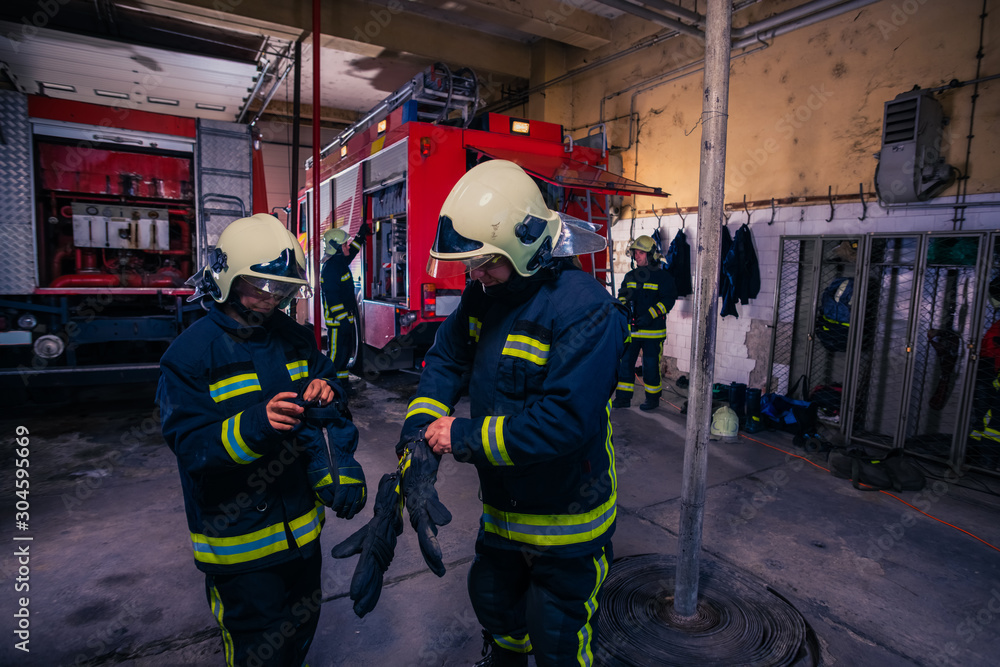 Fototapeta premium Firefighters preparing their uniform and the firetruck in the background inside the fire station