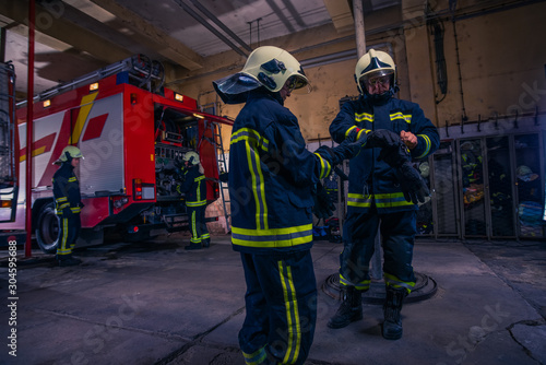 Firefighters preparing their uniform and the firetruck in the background inside the fire station