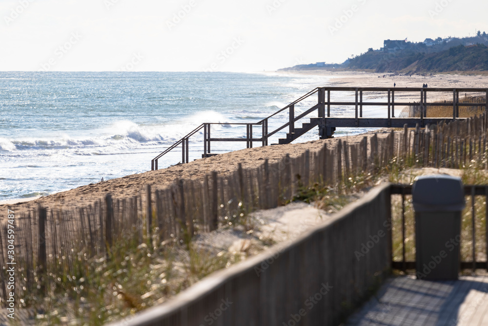 Wooden stairway leads to access of public/private beach, with dune protection fencing in foreground