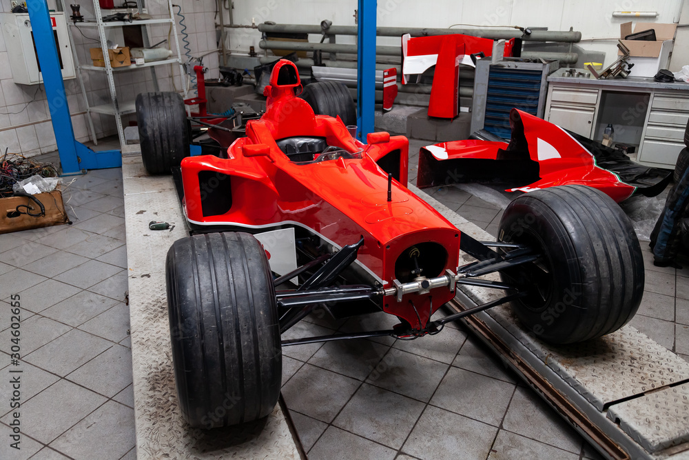 The process of repairing and restoring a red sports car at a pitstop in the service station or a repair workshop on a lift. The process of repairing and restoring a red sports car at a pitstop in the service station or a repair workshop on a lift.