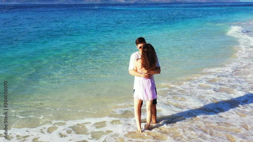 Happy couple hugging and kissing on exotic beach washed by sea waves on a beautiful background with sea, mountains and bright sky in Indonesia Happy couple hugging and kissing on exotic beach washed by sea waves on a beautiful background with sea, mountains and bright sky in Indonesia