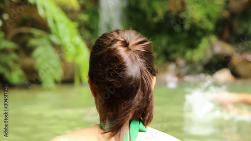 Young brunette girl entering inside relaxing thermal water pool with a waterfall in Caldeira Velha. Furnas, Azores, Portugal. photo