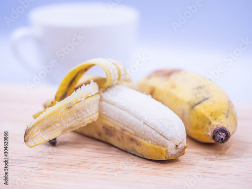 Closeup of couple yellow cultivated banana on wooden cutting board, blurry coffee cup and gray background in the kitchen for healthy eating or dieting concepts and ideas.