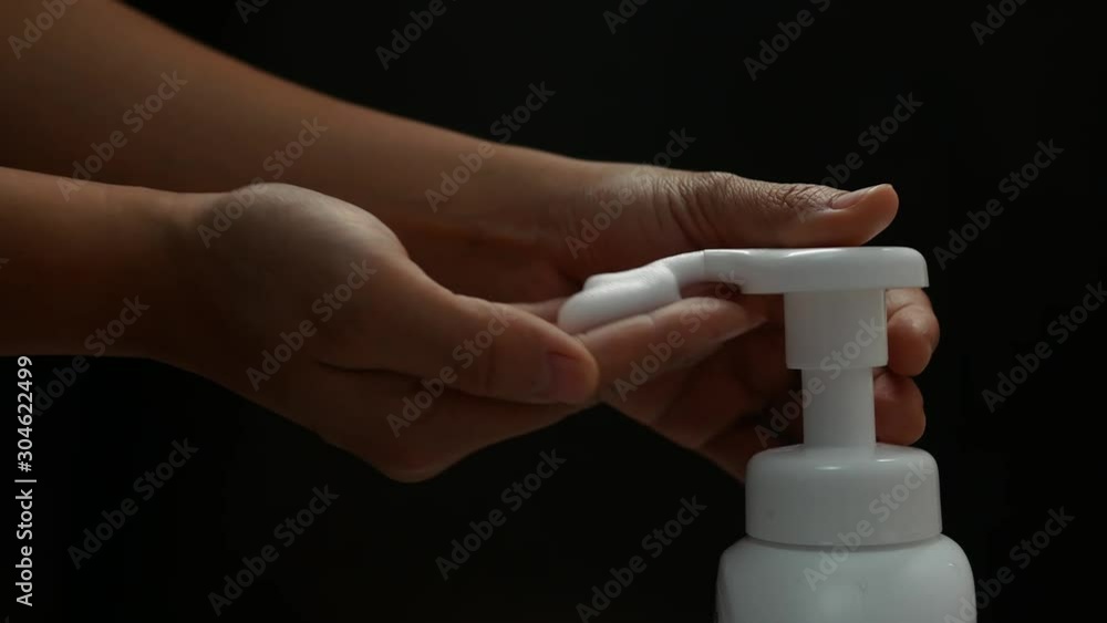 Close up of woman's hand press white plastic pump bottle and other hand take cleaner foam, isolated on black background. Concept of skin care product. Close up of woman's hand press white plastic pump bottle and other hand take cleaner foam, isolated on black background. Concept of skin care product.