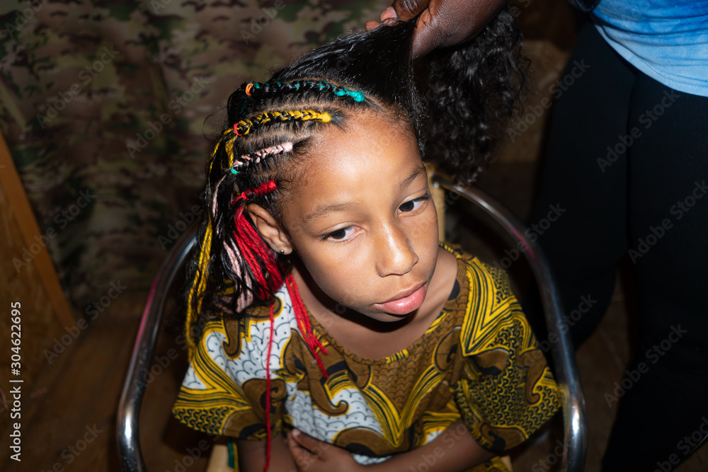 African hairdresser plaits braids with multicolored artificial strands for  mixed Jamaican European ethnicity little girl. Portrait of a child with  curly long hair Stock Photo | Adobe Stock