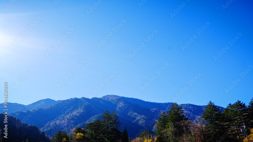 Scenic landscape view of nature forest with  mountain range hills trees and clear blue sky background in fall autumn season of kamikochi, in Hotaka Ranges, Kamikochi, Japan.