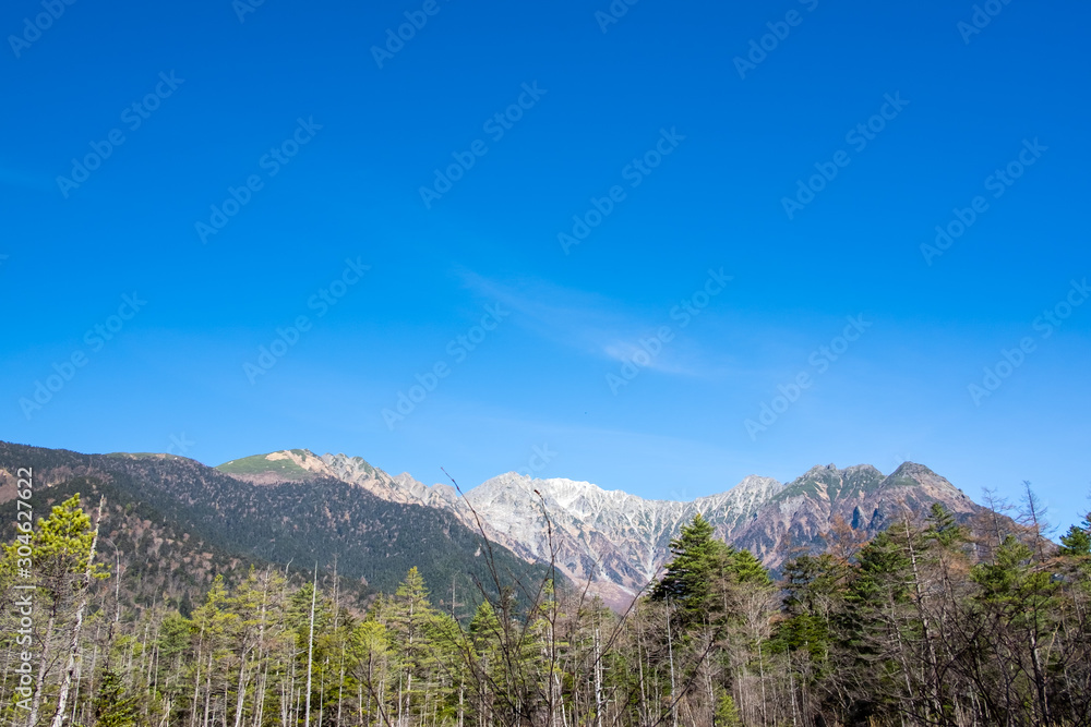 Scenic landscape view of nature forest with white snow mountain hills trees and clear blue sky background in fall autumn season of kamikochi, in Hotaka Ranges, Kamikochi, Japan.