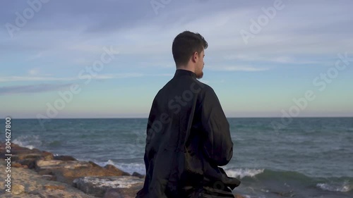 Solow motion of a man, he meditates in tai chi style alone. Tai Chi training at sunset with typical tai chi dress in a colorful day. photo