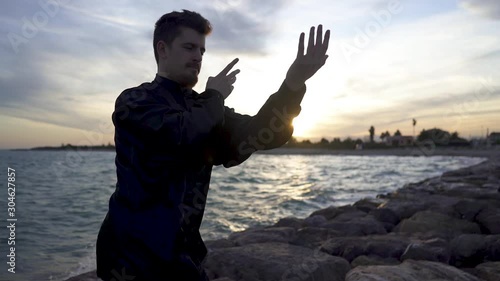 Backlight of the sun in Solow motion of a man, he meditates in tai chi style alone and concentrated. Tai Chi training at sunset with typical tai chi dress. photo