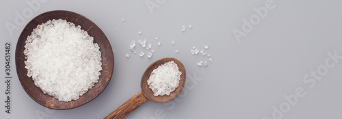 White bath salt in bowl and spoon from coconut shell on gray background. Natural spa products concept. Top view, flay lay, copy space, horizontal banner