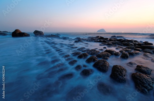 Sunrise scenery at a beautiful rocky beach with unique tofu-like rock formations along the coast in northern Taiwan & an island on the distant horizon under dramatic dawning sky (long exposure effect)