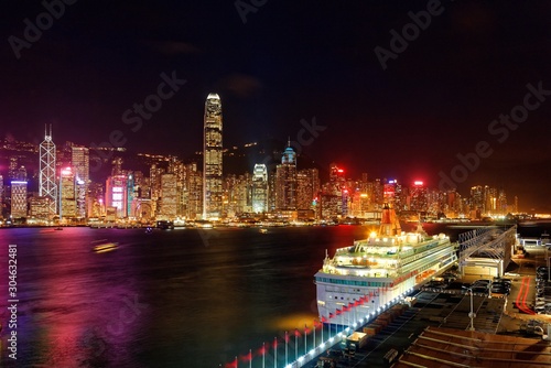 Night scenery of Hong Kong with a skyline of crowded skyscrapers by Victoria Harbor  a luxury cruise liner parking by the pier of Harbour City and lights of high-rise buildings glistening in twilight