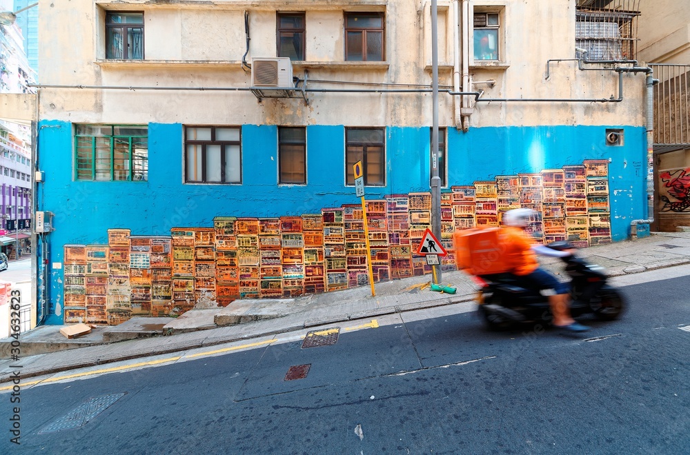 Fototapeta premium A motorcycle courier passing by the famous Graham Street Wall Mural, a colorful street art and a popular Instagram check-in spot in Central District, Hong Kong, China, Asia
