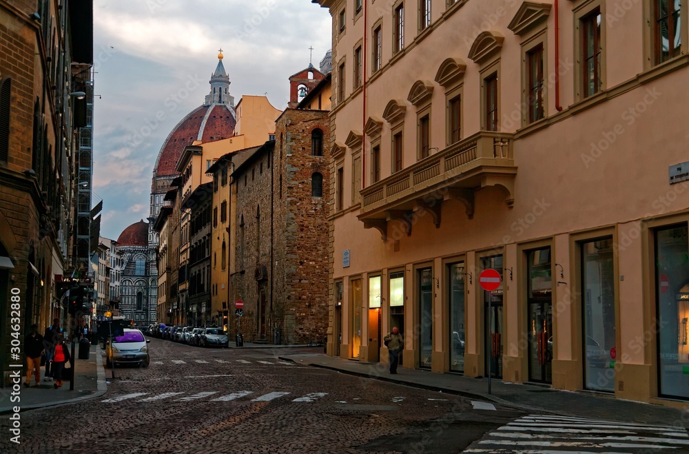 Morning scenery of a narrow cobbled street in the old town of Florence, Italy, with view of a car driving in the alley and the Dome of majestic Cathedral of Saint Mary of the Flowers in the background