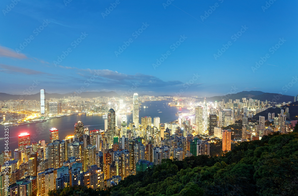Night scenery of Hong Kong viewed from top of Victoria Peak with city skyline of crowded skyscrapers by Victoria Harbour & Kowloon area across the busy seaport ~ Cityscape of Hongkong in blue twilight