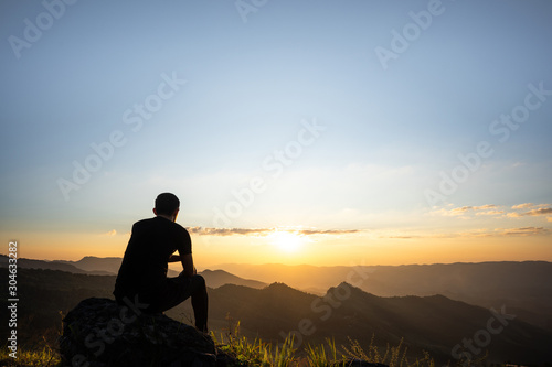 lonely man sitting and relaxing on the rock in front of the beautiful mountain background in sunset.Chilling out freedom on a good time.Summer vacation, happy holidays, travel and people concept.