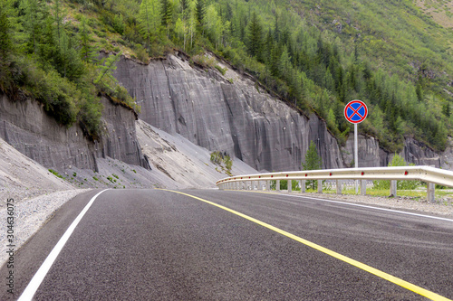 sandy cliffs along the bend of a road covered with asphalt with markings a solid line and a sign prohibiting the stoping