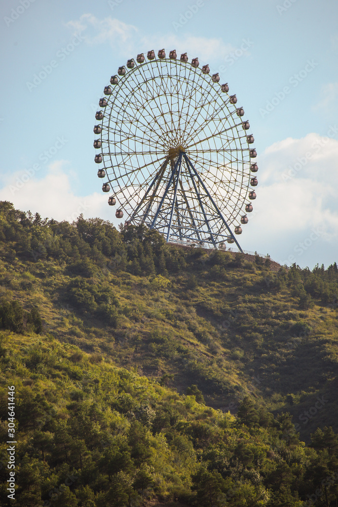 Fototapeta premium Ferris wheel in Tbilisi. Amusement park wheel on top of the hill rising above tbilisi, georgia