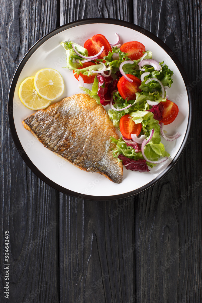 Fried gilt-head fish fillet with a side dish of vegetable salad close-up on a plate. Vertical top view Fried gilt-head fish fillet with a side dish of vegetable salad close-up on a plate. Vertical top view