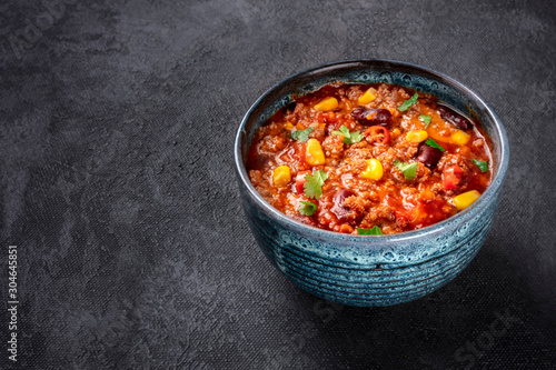 Chili con carne, a Mexican stew with beans, ground meat, corn, and chilli peppers, on a dark background with a place for text