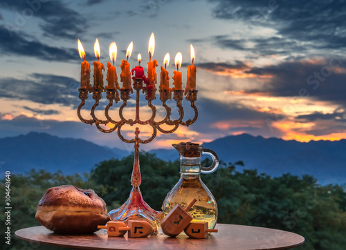 Hanukkah holiday with menorah, burning candles, sweet donut, jar of olive oil...