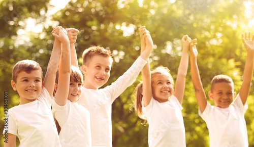 Group of children holding hands up in park on sunny day. Volunteering with kids