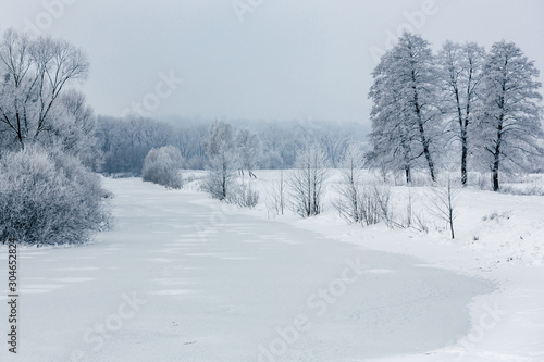 Winter river covered with ice and snow, winter landscape with trees and snow, frost on the trees. Winter landscape. Winter frosty nature in the morning sunlight.