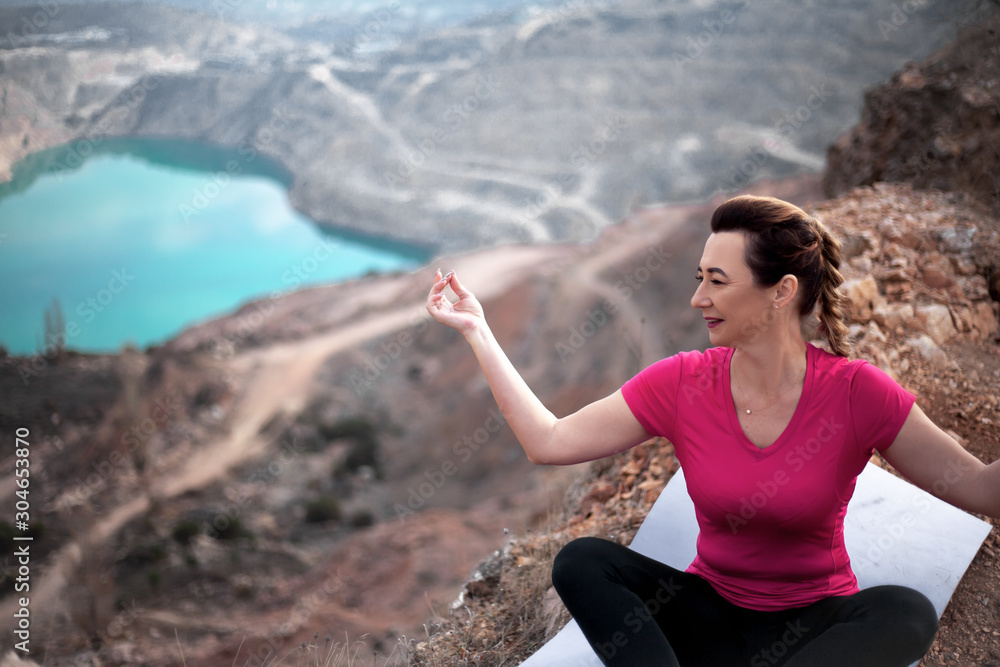 40s years woman dressed sportswear, pink topic and black fitness leggings, sit in yoga pose in harmony herself  outdoor against the heart shaped  quarry .