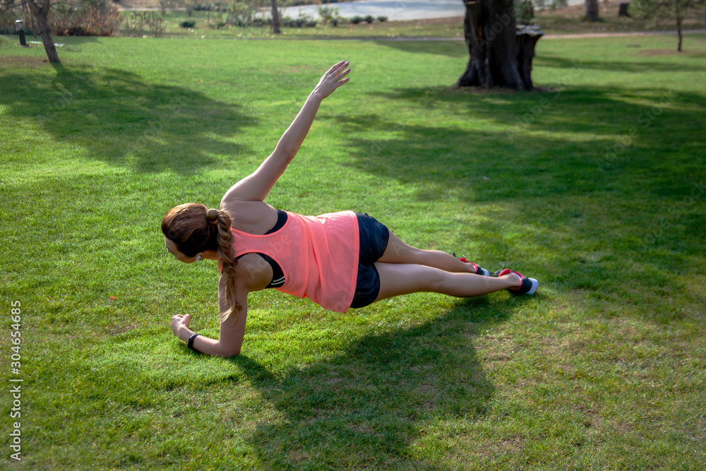 Fototapeta premium Mature 40s years old woman leads a healthy lifestyle outdoor on the green grass at the park. Middle aged sport and active female dressed sportswear practice fitness exercise
