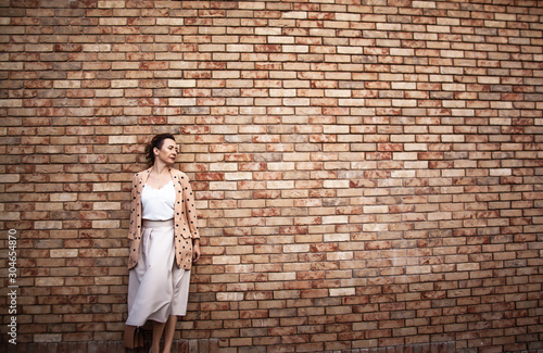 Middle-aged woman dressed elegant offive style skirt , white silk shirt and pea jacket posing against the street brick wall