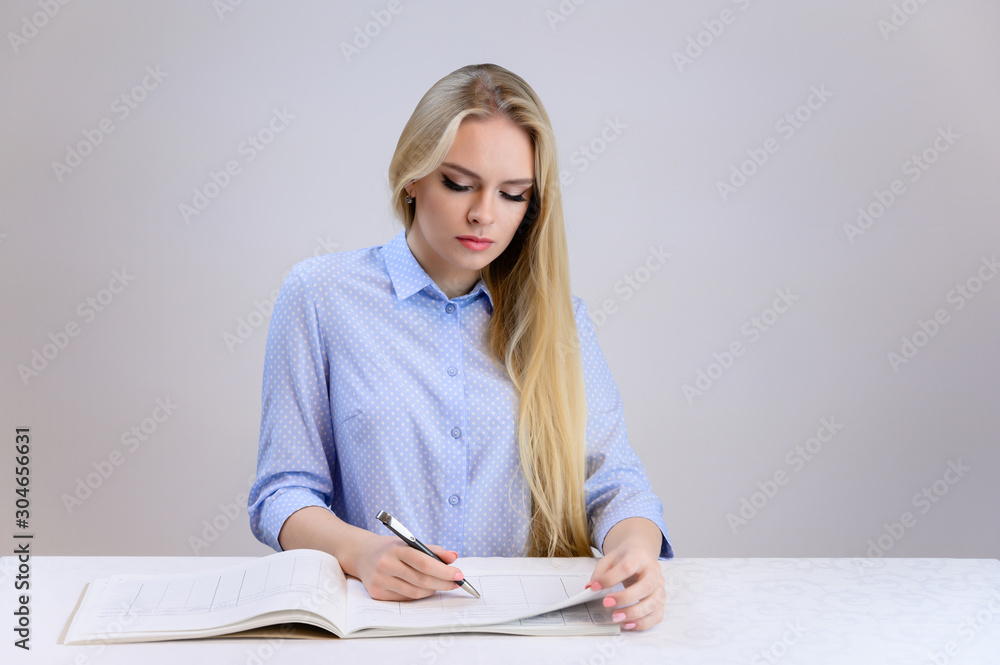 Concept cute model student secretary works sitting at a table. Close-up portrait of a beautiful blonde girl with excellent makeup with long smooth hair on a white background in a blue shirt. Concept cute model student secretary works sitting at a table. Close-up portrait of a beautiful blonde girl with excellent makeup with long smooth hair on a white background in a blue shirt.