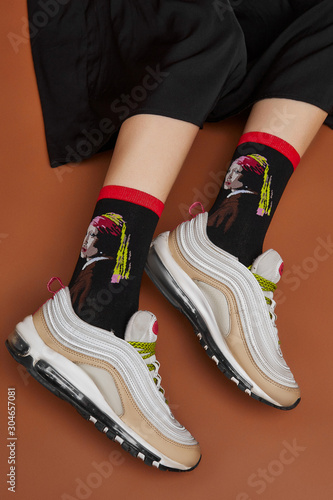 Φωτογραφία Cropped shot of a girl's foots in white sneakers, lying on a brown background